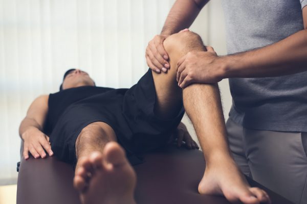 Male therapist massaging knee of athlete patient - sport physical therapy concept